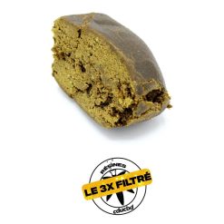 Un morceau de résine brune, légèrement effrité, avec une étiquette « Le 3x Filtré ».
