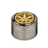Grinder métallique argenté avec un couvercle orné d'une feuille de cannabis dorée en strass, entourée de pierres brillantes.